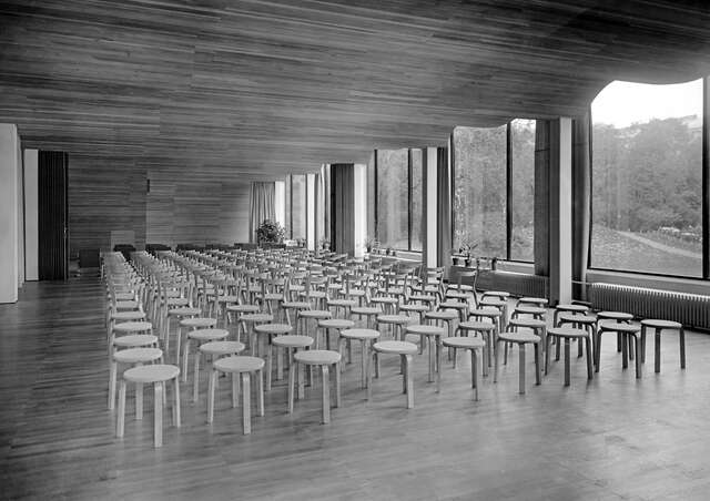 Auditorium with a curved wooden ceiling and few hundred Aalto stools on the floor.