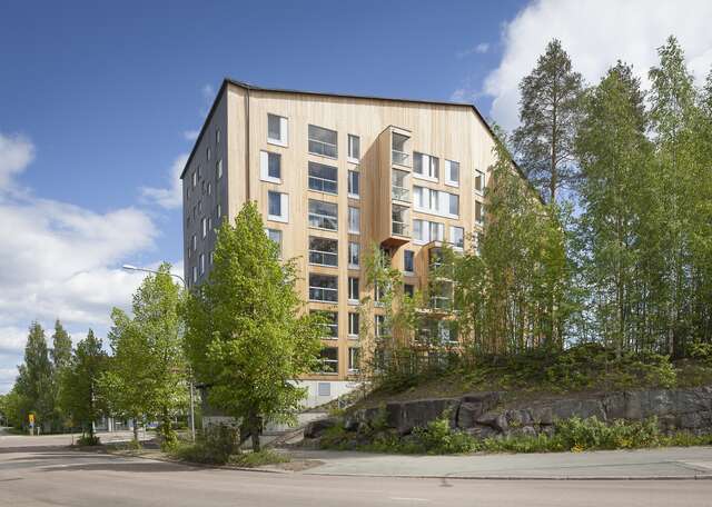 Apartment building with a wooden exterior and gable roof, around the building there are many trees.