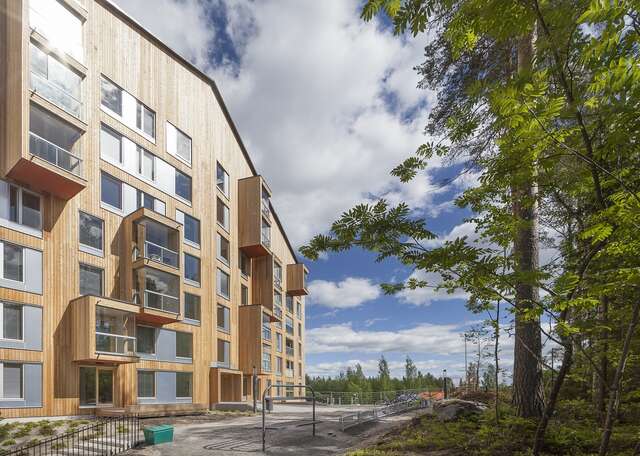 Apartment building with a wooden exterior and gable roof, around the building there are many trees.