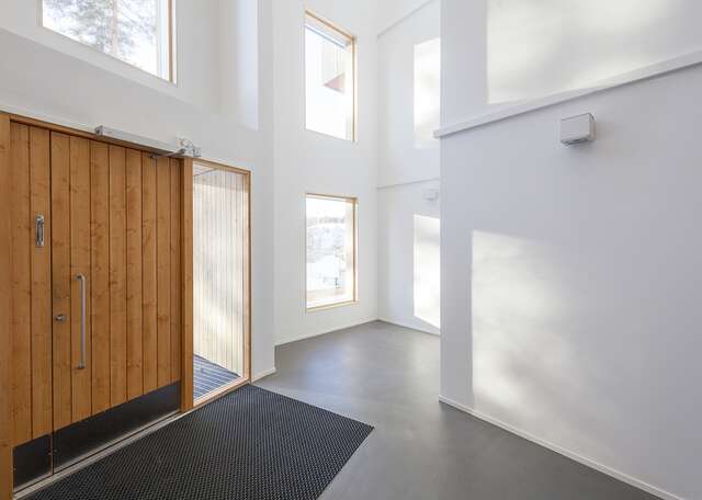 Entrance with white walls, large windows and a wooden door leading to the outside of the building.