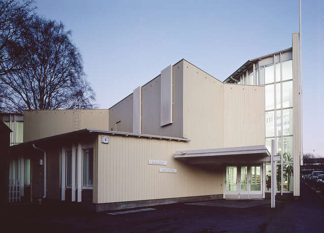 Cream colored facade with white beam details and a tall glazed wall.