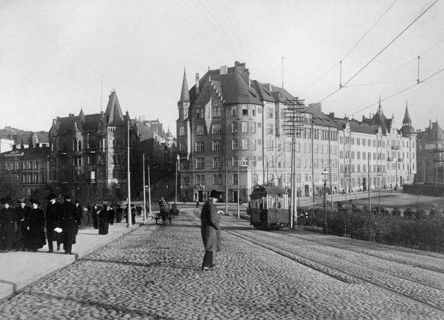 Black and white picture of the multiple storey building facade wit pedestrians walking along the street.