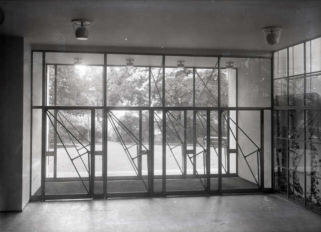 4 glass doors with triangular metal details in an entrance hall next to a window to the stairway.