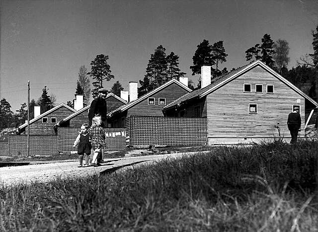row of wooden houses, a father and two small children walk on the road in front of them.
