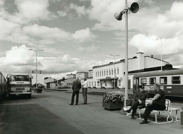 Railway station, two men sitting on a bench, two men standing behind
