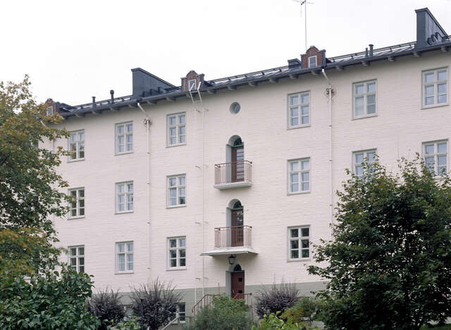 Three-storey light-coloured building with a garden in the foreground