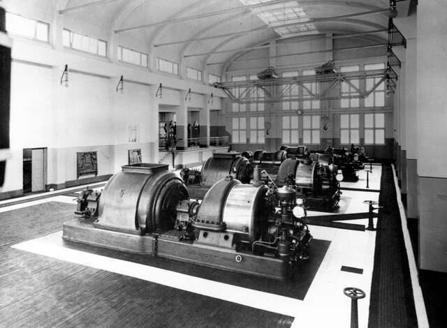 Power plant machinery in an industry hall with three large windows in the background