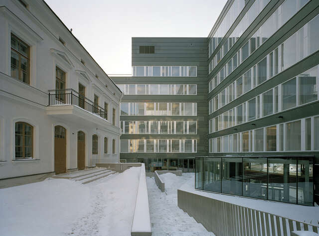 Juxtaposition between a grey modern office building on the right and a white villa on the left.