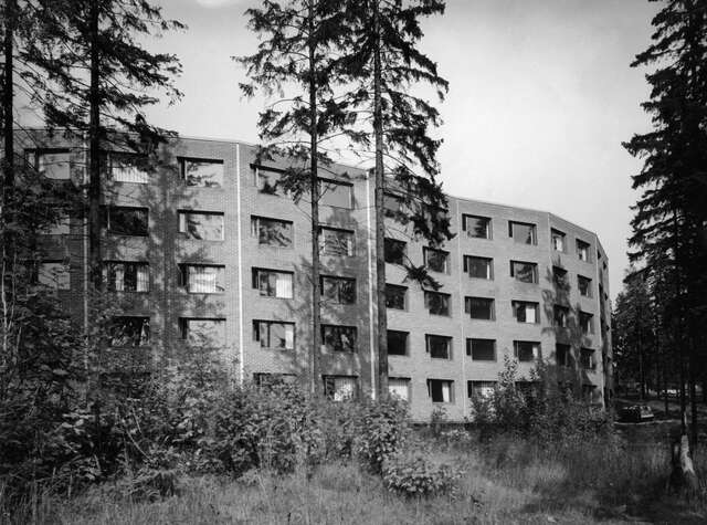 Five-storey brick-building with trees and bushes in the foreground