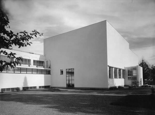 Black and white picture of a white building with a lower wing at the left side and black framed windows.
