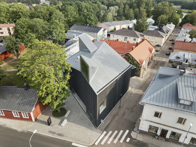A black wooden building in the middle of a town as seen from the air.