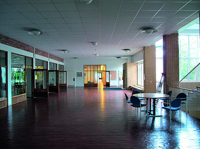Entrance hall with a brown tile floor, a small seating area, doors leading to other parts of the school and stairs at the right.