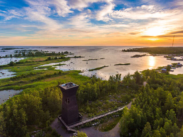 Aerial view in evening sun, a wooden observation tower in the front ground, scattered strips of land in the sea