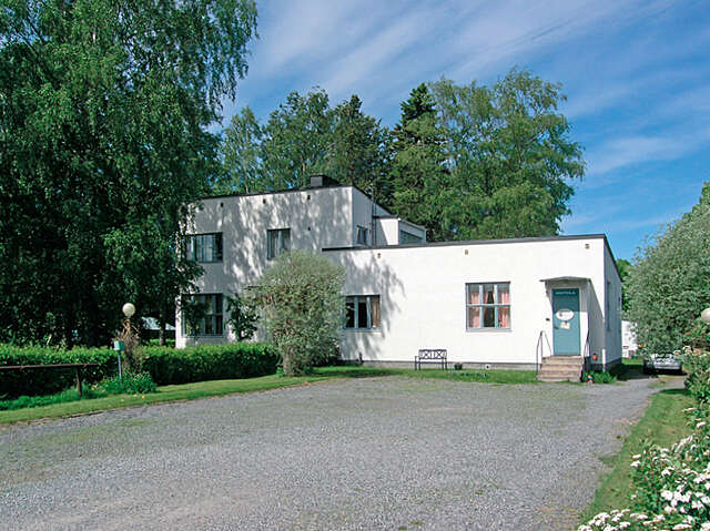 Simple white building with light blue window frames and doors with a garden around it on a sunny day.