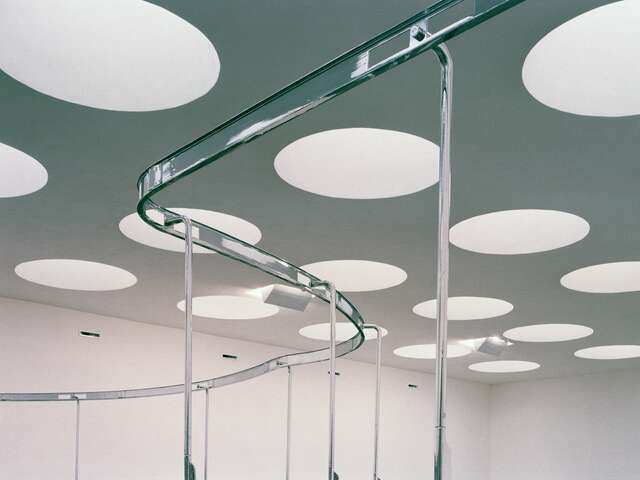 Ceiling with large circular windows in rows, a metal railing in the foreground of the image.