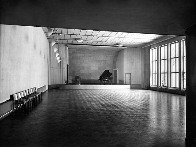 bare festival hall with 10 chairs pushed the left wall and a grand piano on the stage.