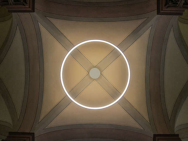 Circular light hanging from a groin vault ceiling.