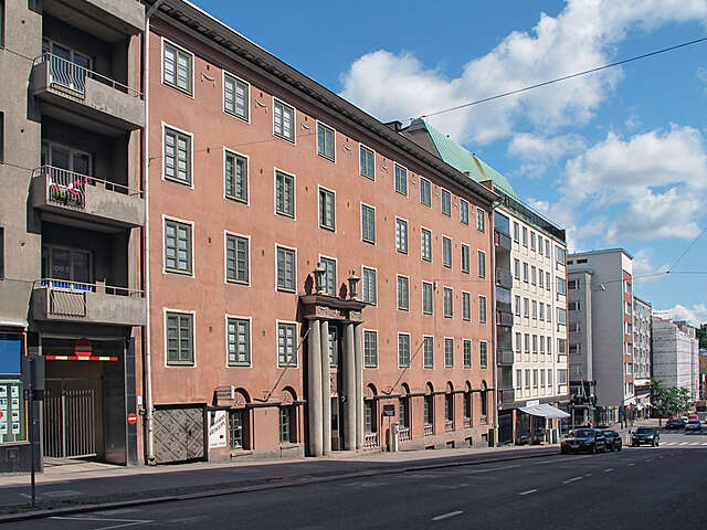 Apartment building with 4 rows of grid windows , decorative pillars at the entrance and a storefront at street level.