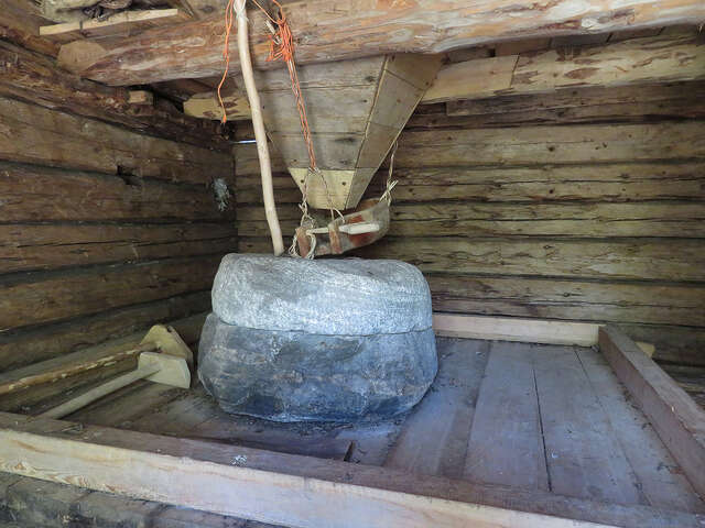 Inside a log building, a carved stone block in the middle, a wooden funnel hanging above