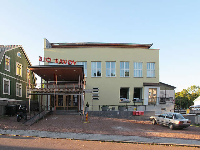 Yellow facade of the Bio savoy cinema with a red sign on the roof and parking spaces at the front.