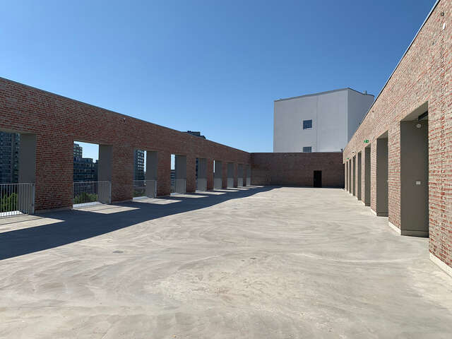 Large outdoor level of building. Concrete floor and brown brick walls on both sides. No ceiling, which reveals this to be the roof of the building.