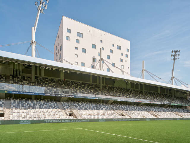 Empty stands of a football stadium, with a towering apartment building seen behind the stands.
