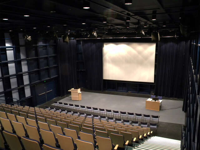 Dark hall with a white screen and a stage in the front.