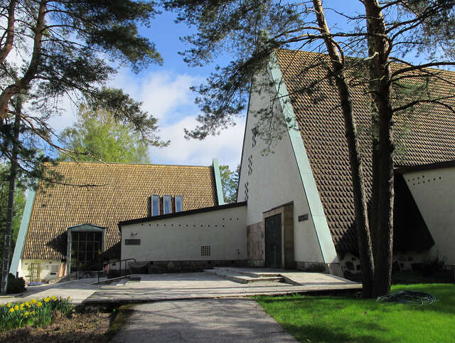 Chapel with a triangular facade and stone artwork depicting people on its wall, steps at the front lead into the chapel.