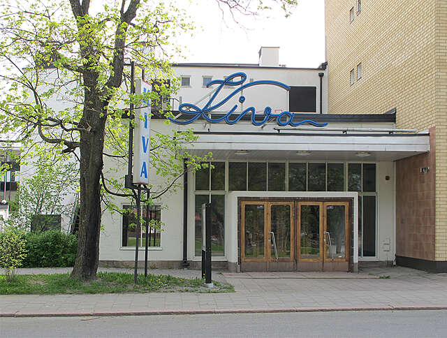 Entrance to the Kiva cinema with a white facade, a grid window wall and wooden doors, the blue Kiva sign is positioned above the entrance.