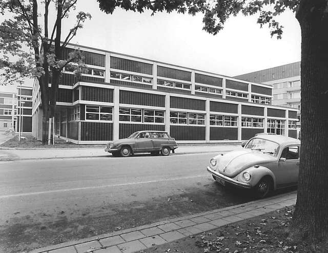 Street view of the. facade with tile and plaster elements and two old cars at the side of the street.