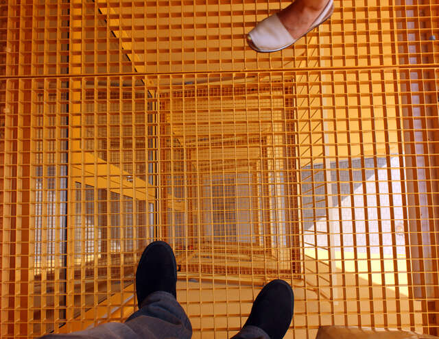 Two people standing on an orange metal net balcony with a view through the other balconies.