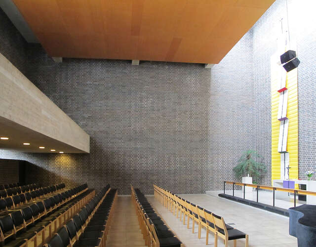 Inside a cube-like space with pews, altar and skylight