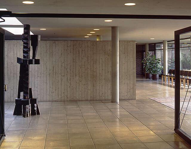 A lobby with concrete surfaces and a wooden sculpture