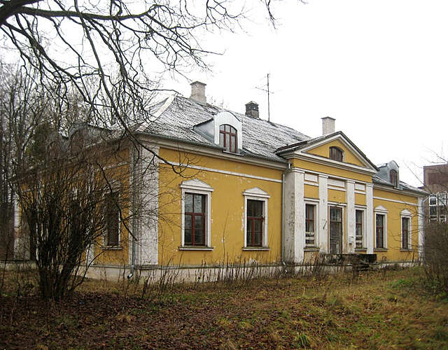 Old yellow house with white decorative elements and grid windows on an autumnal day.