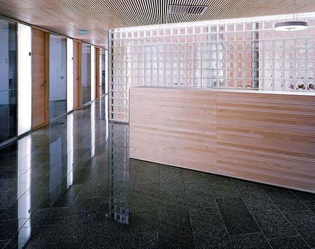 Light wooden reception desk in front of a wall made of glass tiles.