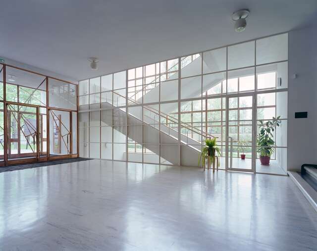 Entrance hall with a glass wall and door leading to the white stairway with wooden railings.