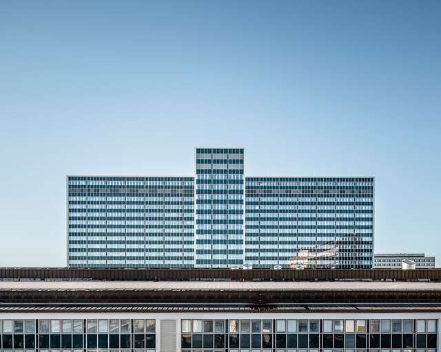 Facade of a multiple story building with rows of windows and glass panels creating a striped look.