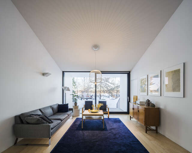 A room with a couch and a sideboard. A large window at the end of the room.