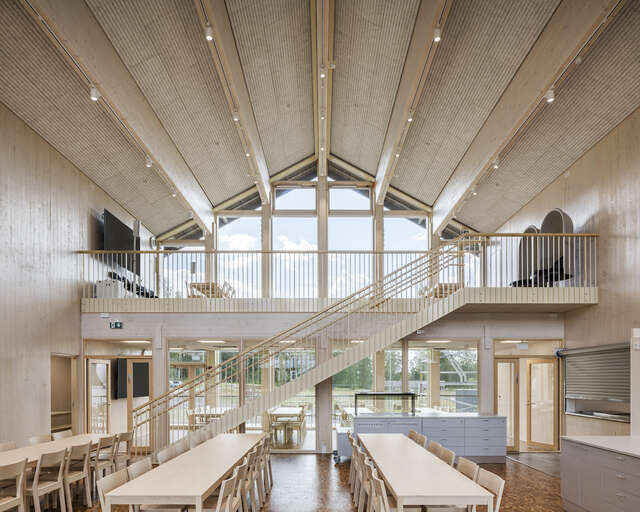 The interior of a wooden structure, with large windows giving natural light. Two rows of tables can be seen inside.