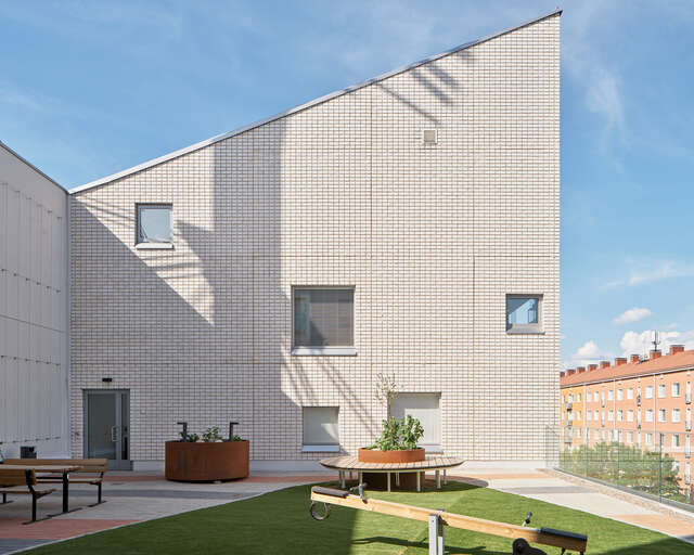Large roof terrace of a building, and a wall of the buildings other side that has five different square windows.