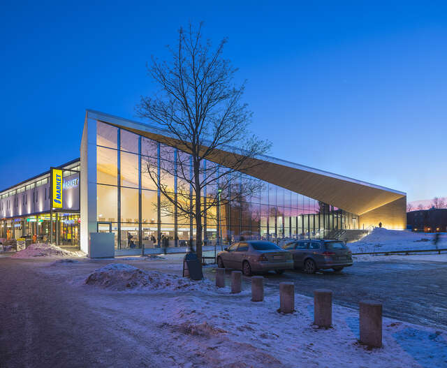 Glass and wood facade of the building on a dark winter afternoon, a supermarket is visible behind the library.
