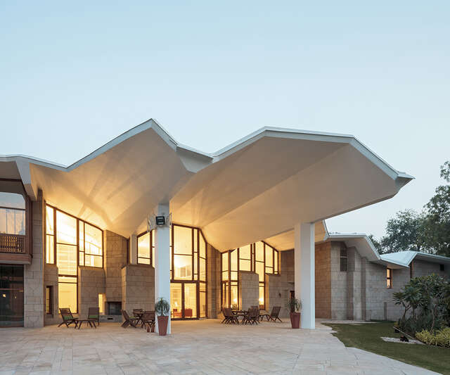 Entrance to the embassy through glass doors, the entrance is covered by the extending white roof that has a complex shape.