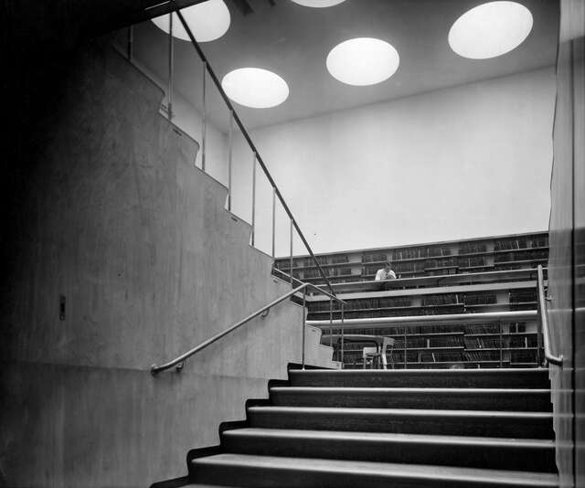 Wooden sides of the stairs with a view towards the bookshelves and the ceiling with large circular ceiling windows.