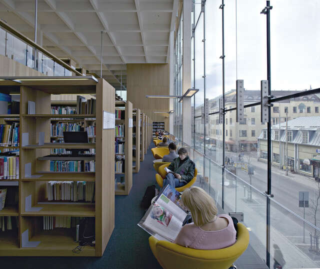 Yellow armchairs between bookshelves and glass wall.