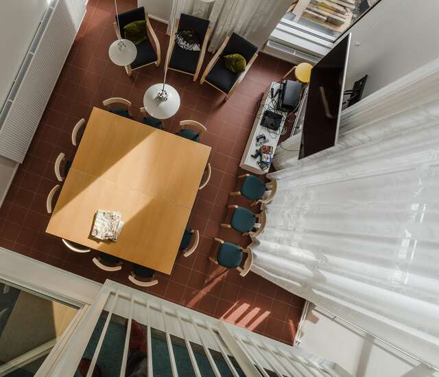 large table and 12 chairs on a red rile floor, armchairs and a TV are positioned at the sides of the room.