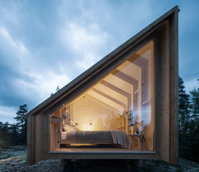 Triangular wooden structure with large window showing a bedroom inside.