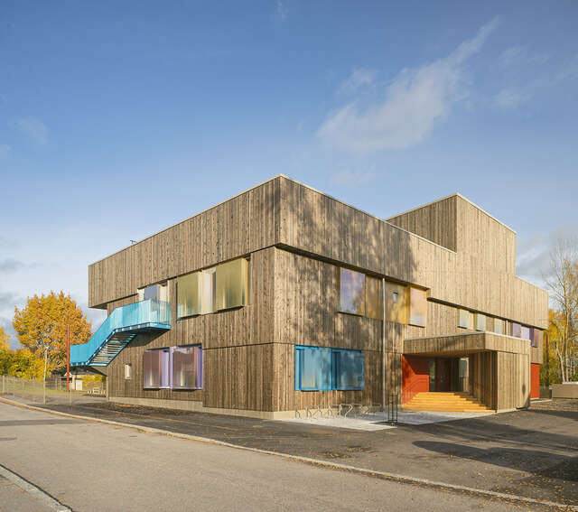 Wooden building with colored window frames and blue stairs outside.
