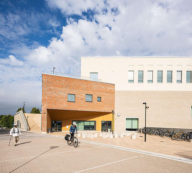 One person cycling nearby a school building and one person walking nearby it.