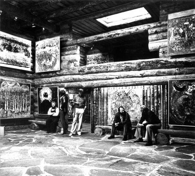 Black and white picture of men sitting in a room full of paintings.