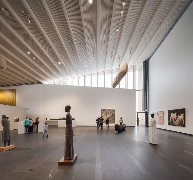 Sculptures of humans and paintings in a large room with a high ceiling.